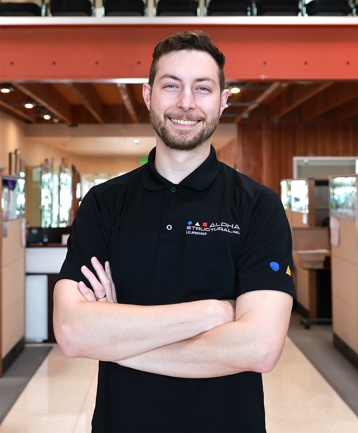 Smiling man in black polo shirt standing confidently.