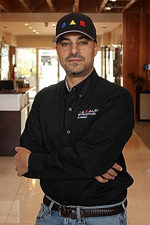 Man in black shirt and cap, confident stance.