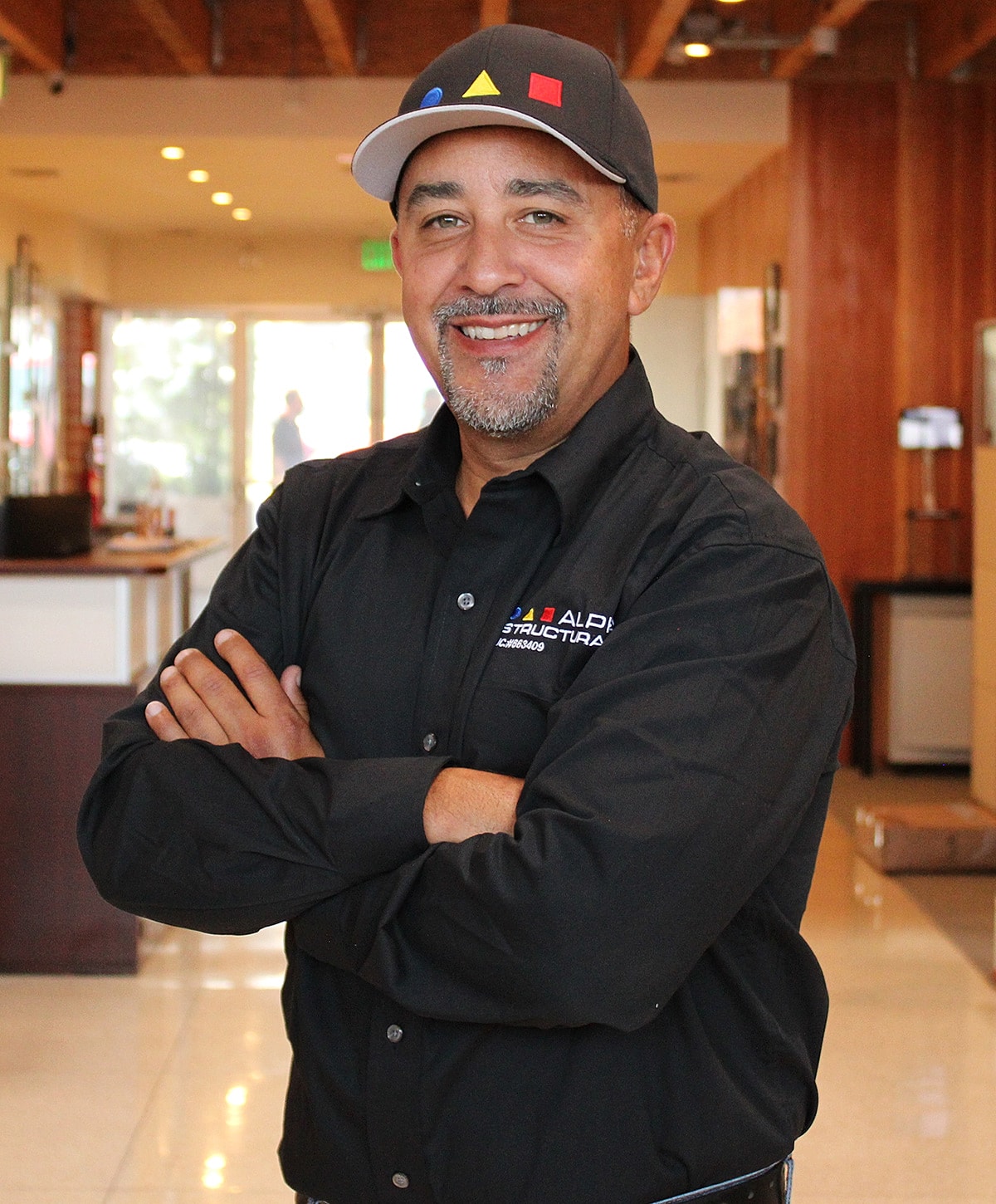 Smiling man in a black shirt with folded arms.