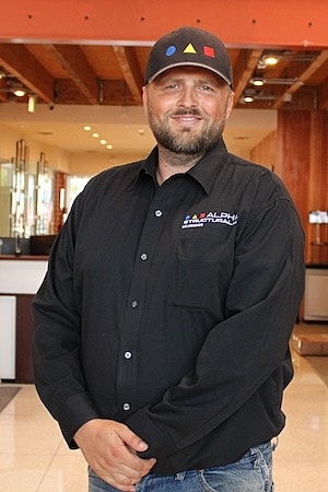Man in black shirt and cap smiling indoors.