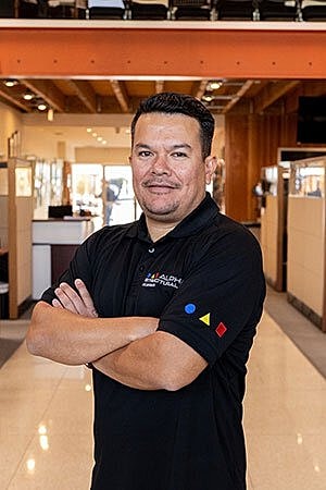Man in black polo standing confidently indoors.