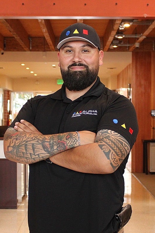 Man with tattoos, black shirt, and cap.