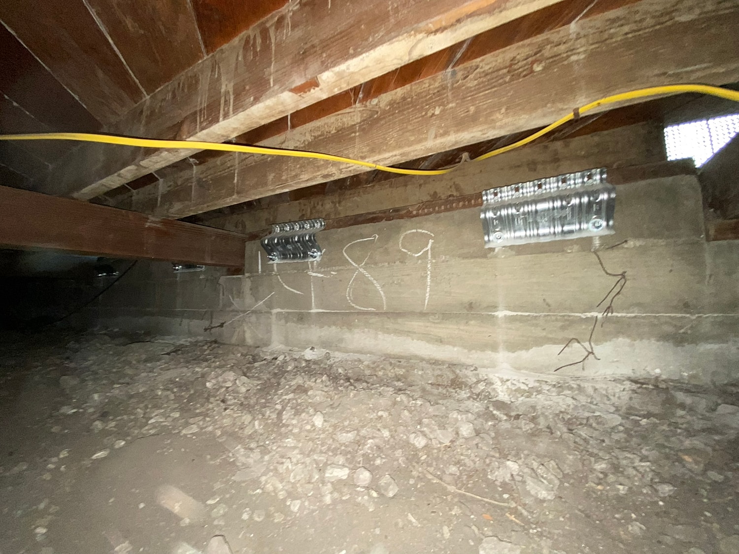 Crawl space with wooden beams and metal brackets.