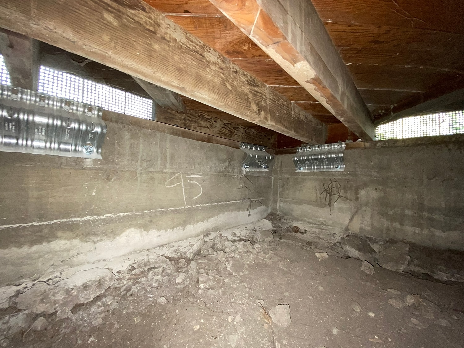 Underfloor view with structural supports and dirt.