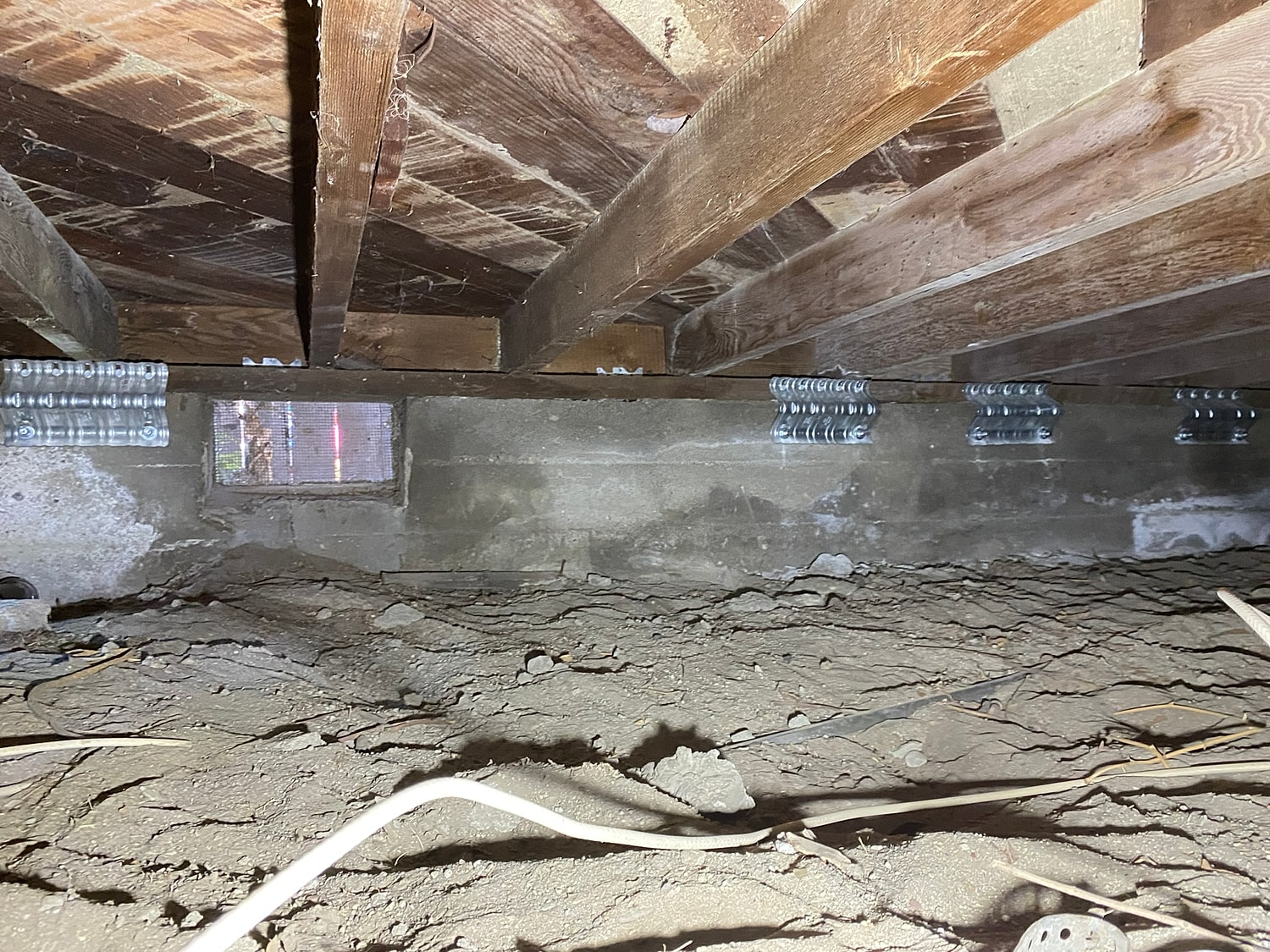 Crawl space with wooden beams and dirt floor.