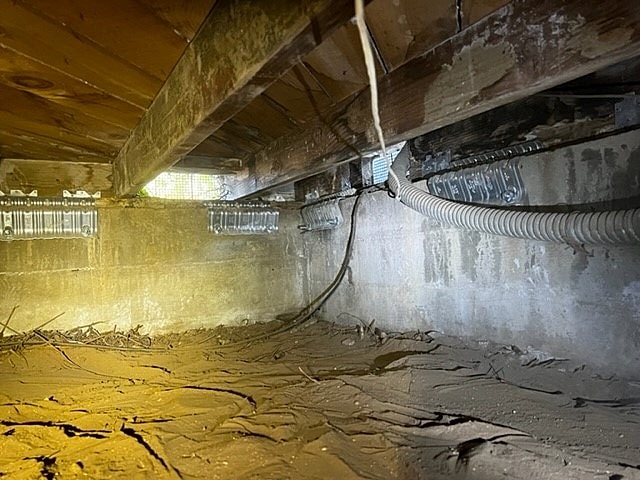 Underneath a house, showing dirt and wires.