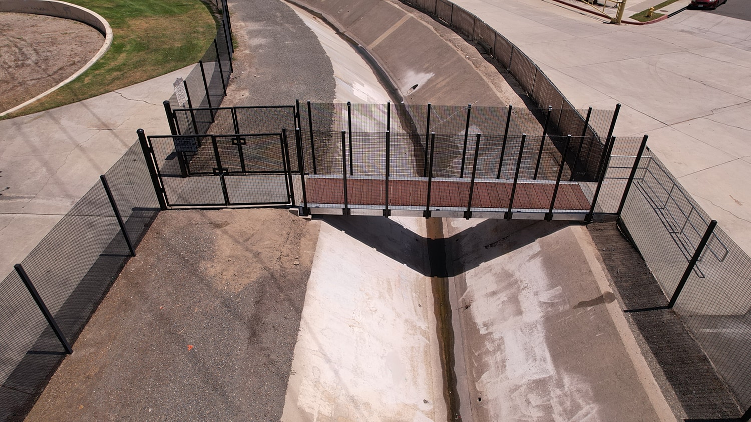 Pedestrian bridge over drainage area with fences.