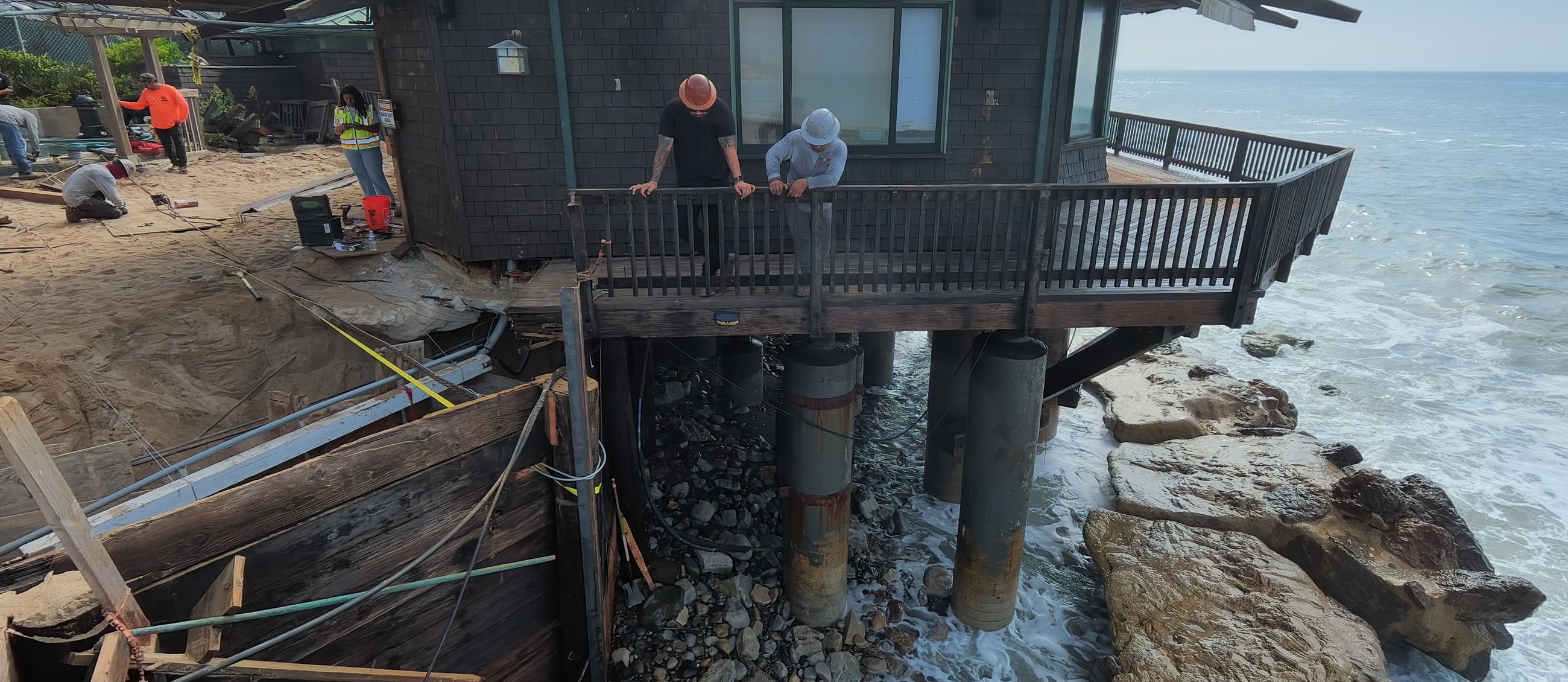Construction workers assess eroded shoreline home stability.