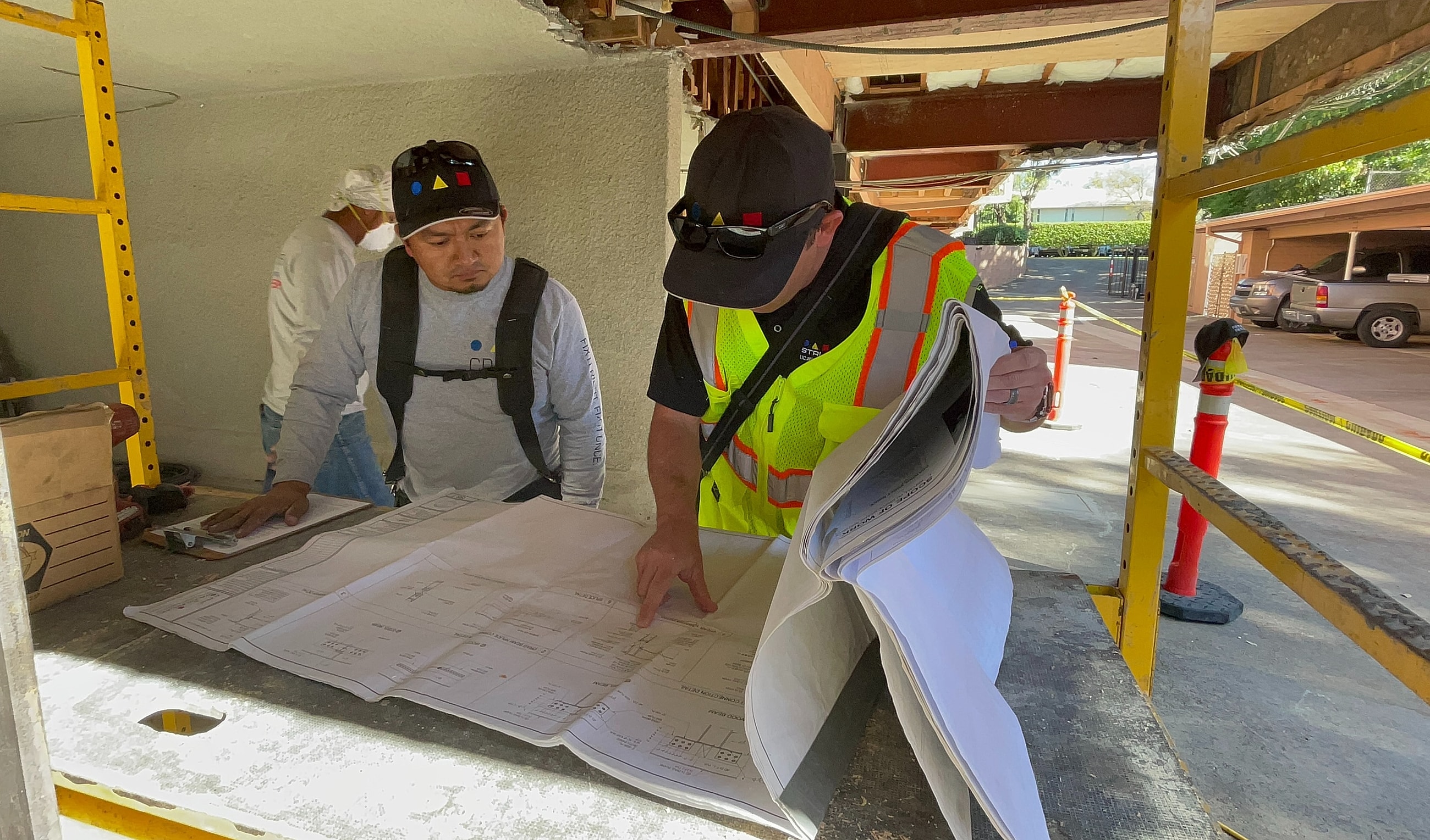 Two workers reviewing construction plans at site.