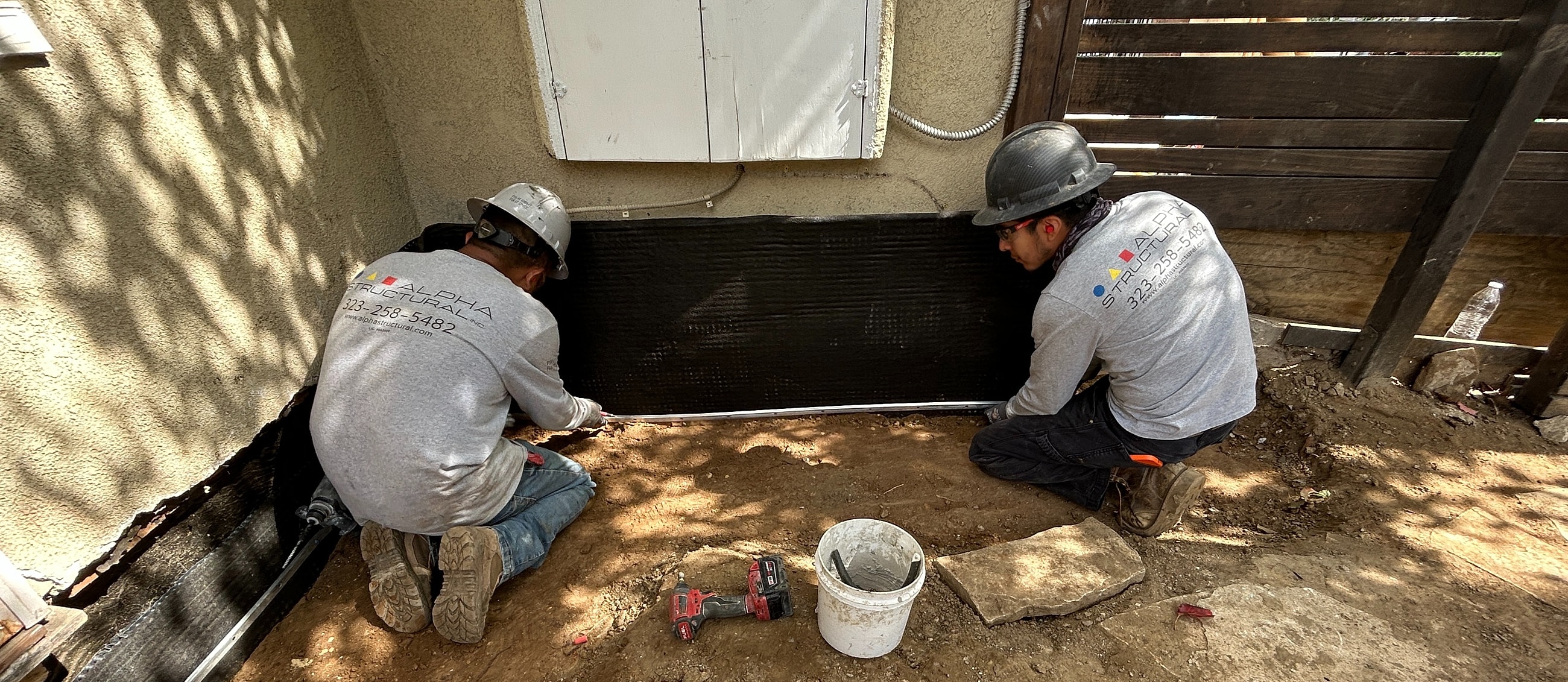 Workers applying waterproofing membrane outside a building.