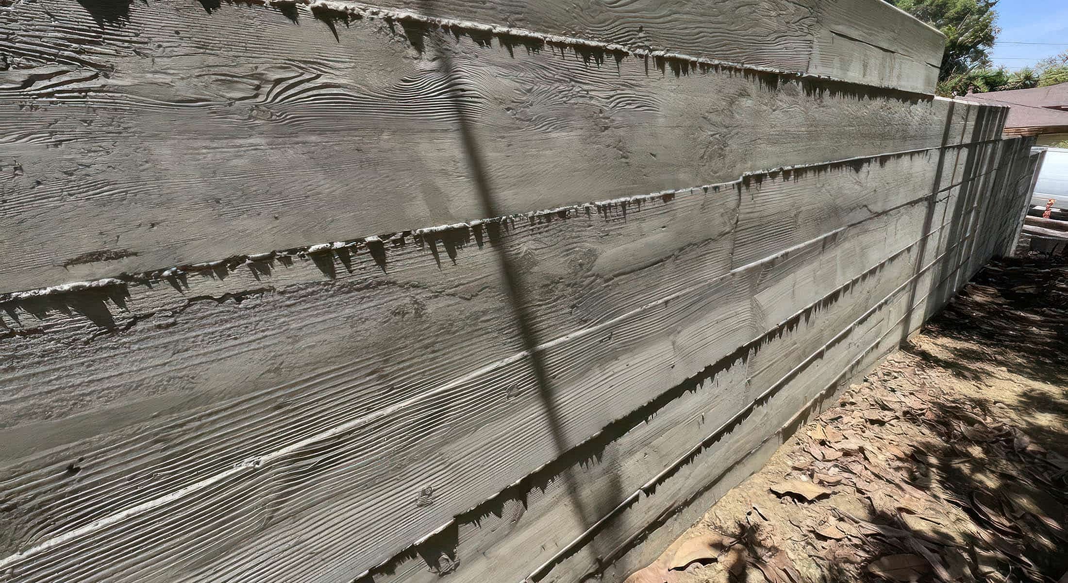 Wooden fence in sunlight next to dry leaves.